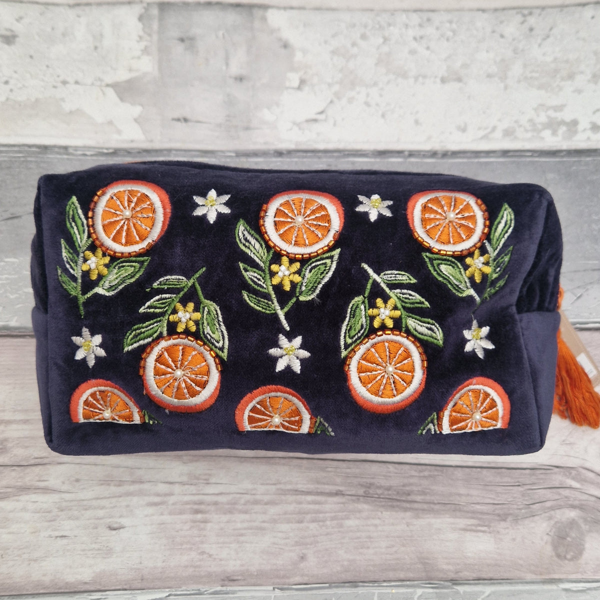A navy blue velvet pouch decorated with embroidered orange slices, green leaves, and small white flowers, resting on a light gray wooden surface.