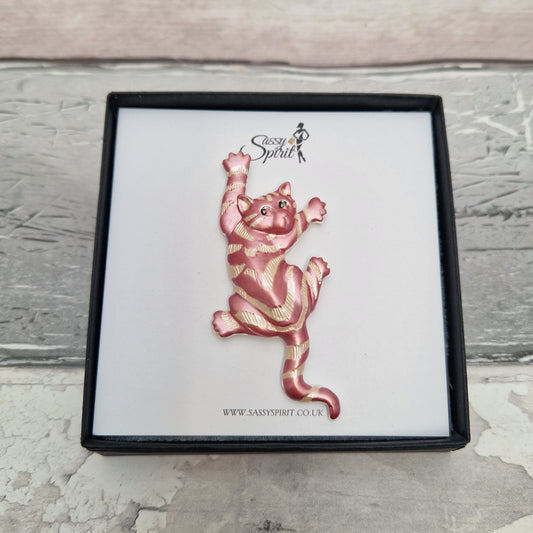 Pink and gold cat-shaped brooch in a black box on a light wooden surface