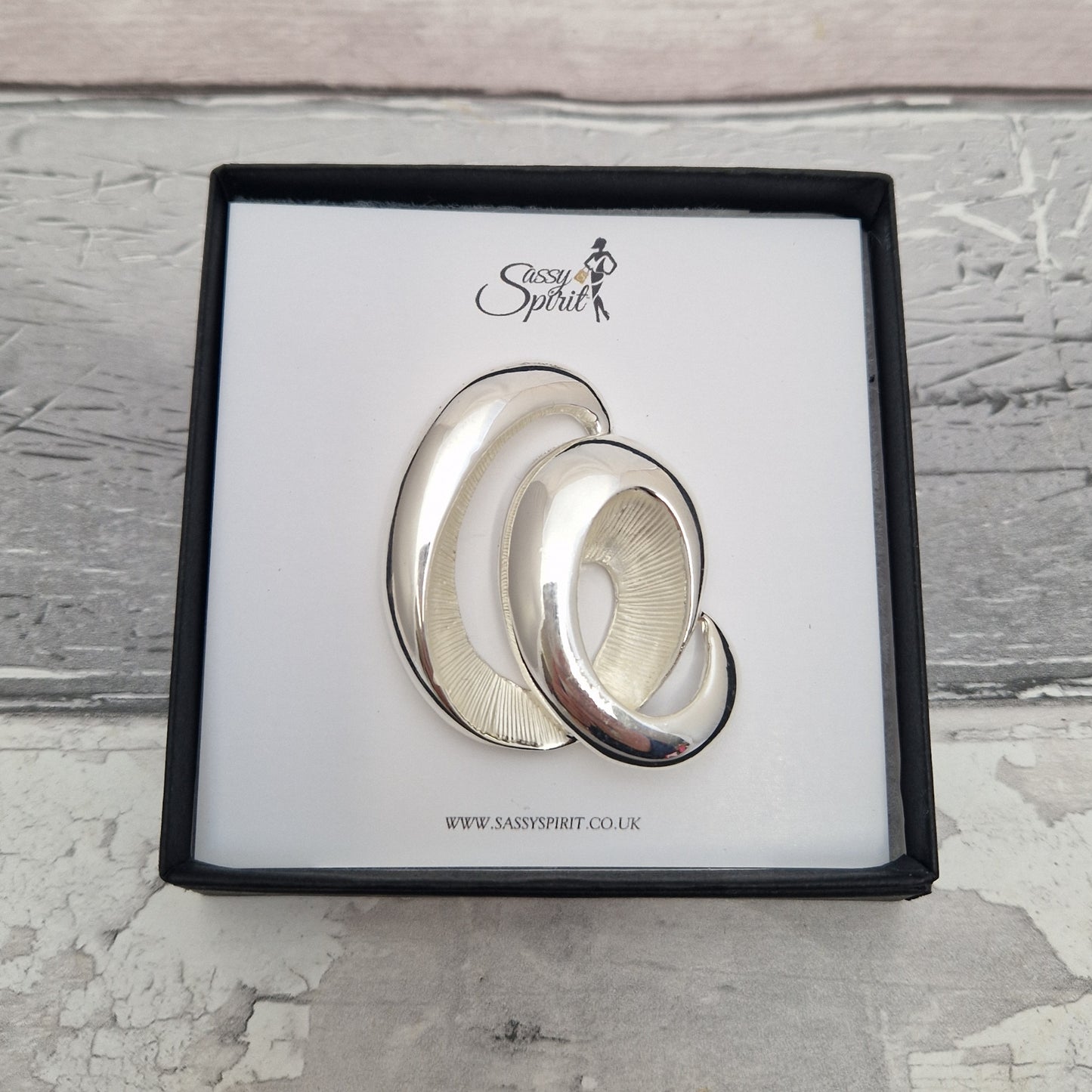 Silver wave magnetic brooch with 'Sassy Spirit' branding on a textured surface