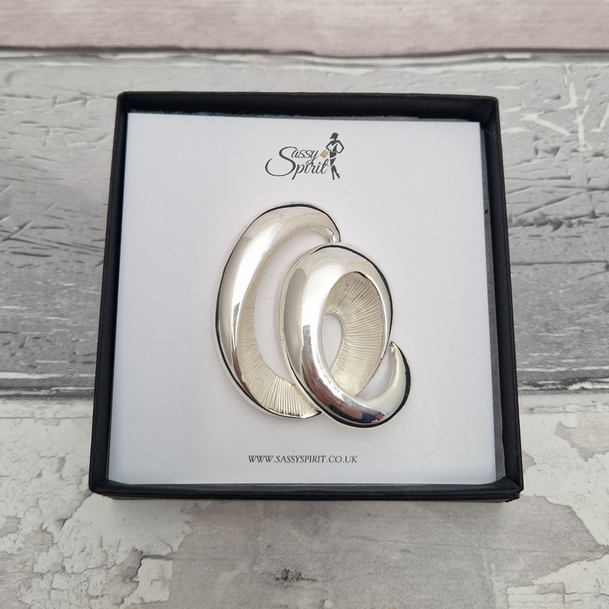 Silver wave magnetic brooch with 'Sassy Spirit' branding on a textured surface