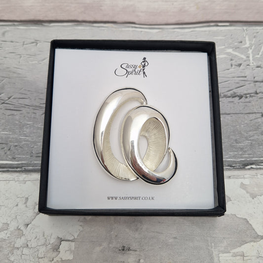 Silver wave magnetic brooch with 'Sassy Spirit' branding on a textured surface