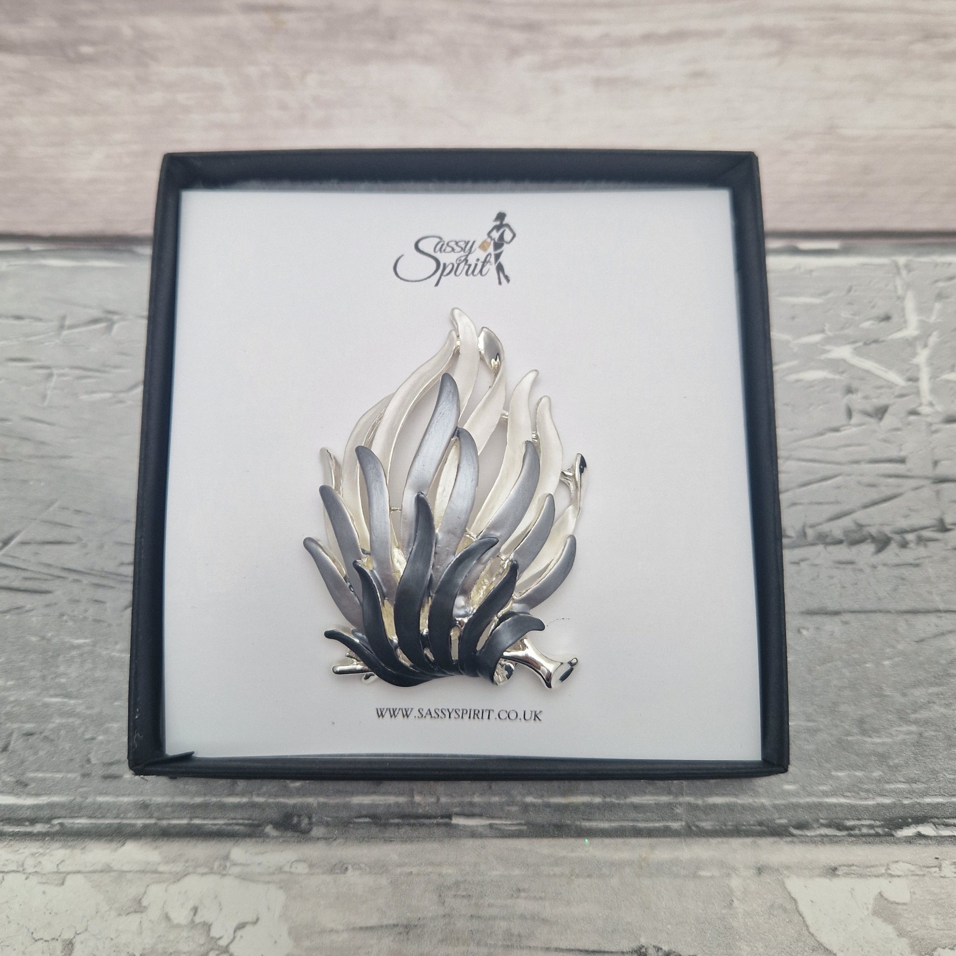 Silver and black fire flames brooch on a branded card with a wooden background