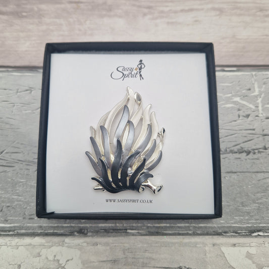 Silver and black fire flames brooch on a branded card with a wooden background