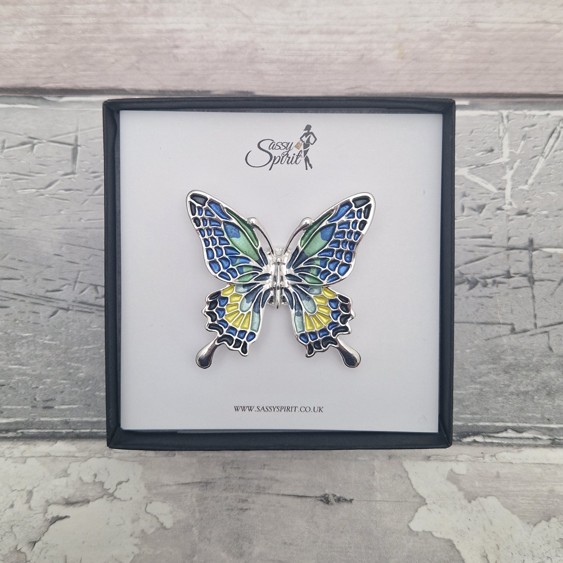 Butterfly-shaped brooch in a black gift box with 'Sassy Spirit' branding on a textured grey background.