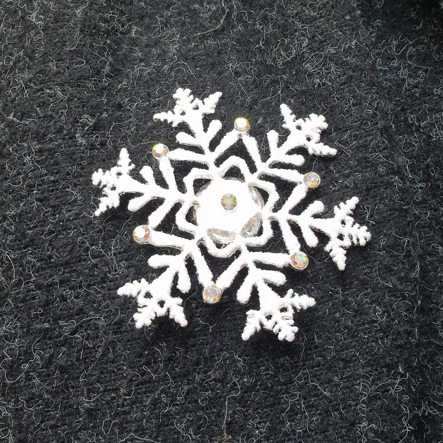 White snowflake brooch with rhinestones on a black textured background