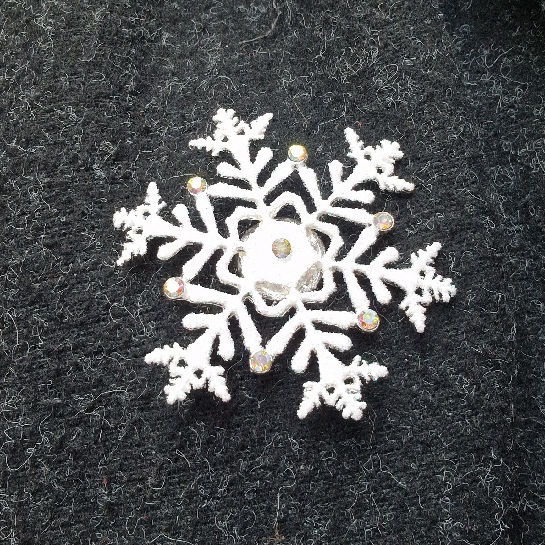 White snowflake brooch with rhinestones on a black textured background