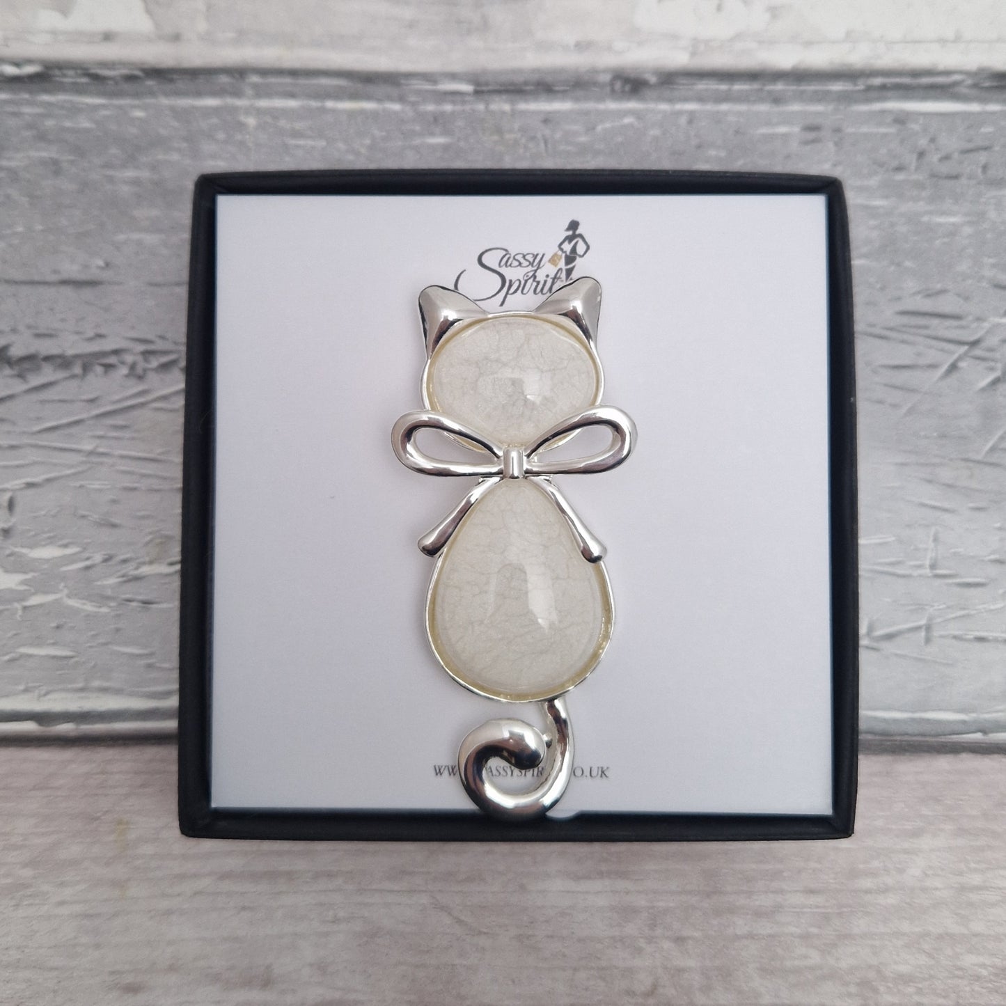 Cat-shaped brooch with a bow on a branded card against a wooden background