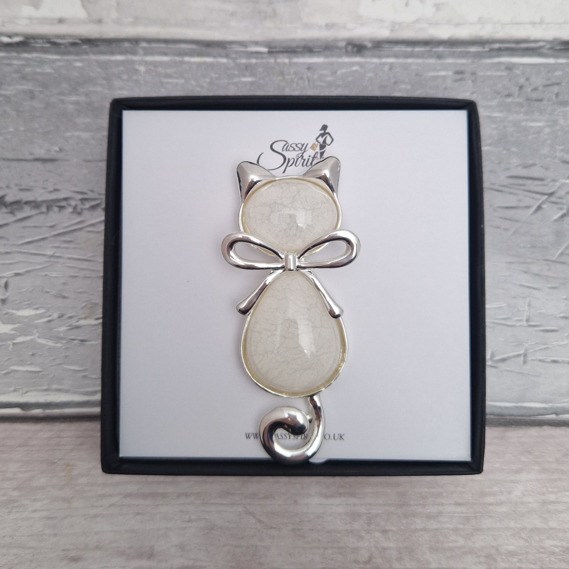 Cat-shaped brooch with a bow on a branded card against a wooden background