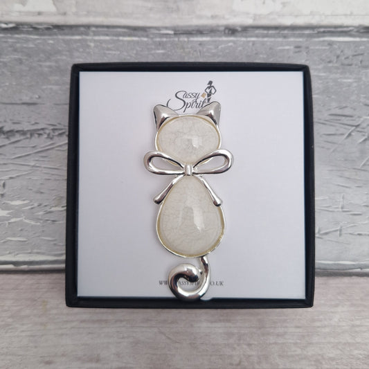 Cat-shaped brooch with a bow on a branded card against a wooden background