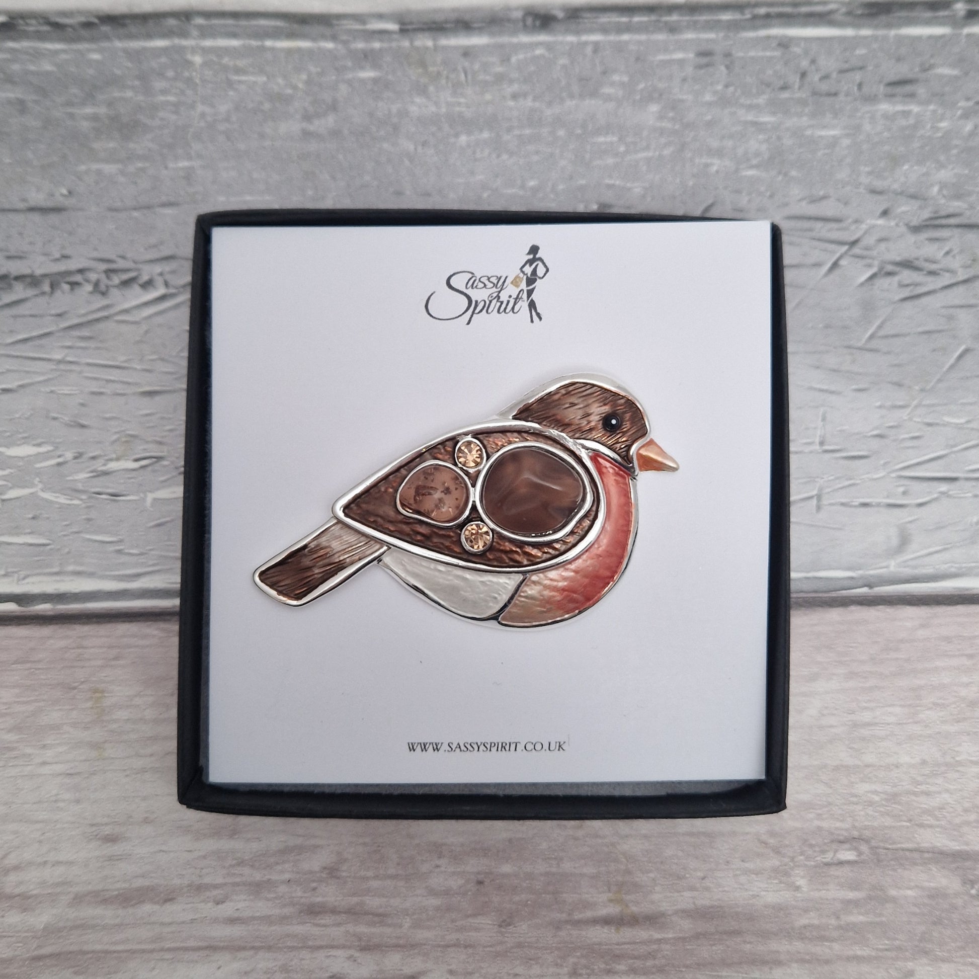 Bird-shaped brooch on a branded card with 'Sassy Spirit' logo on a wooden surface.