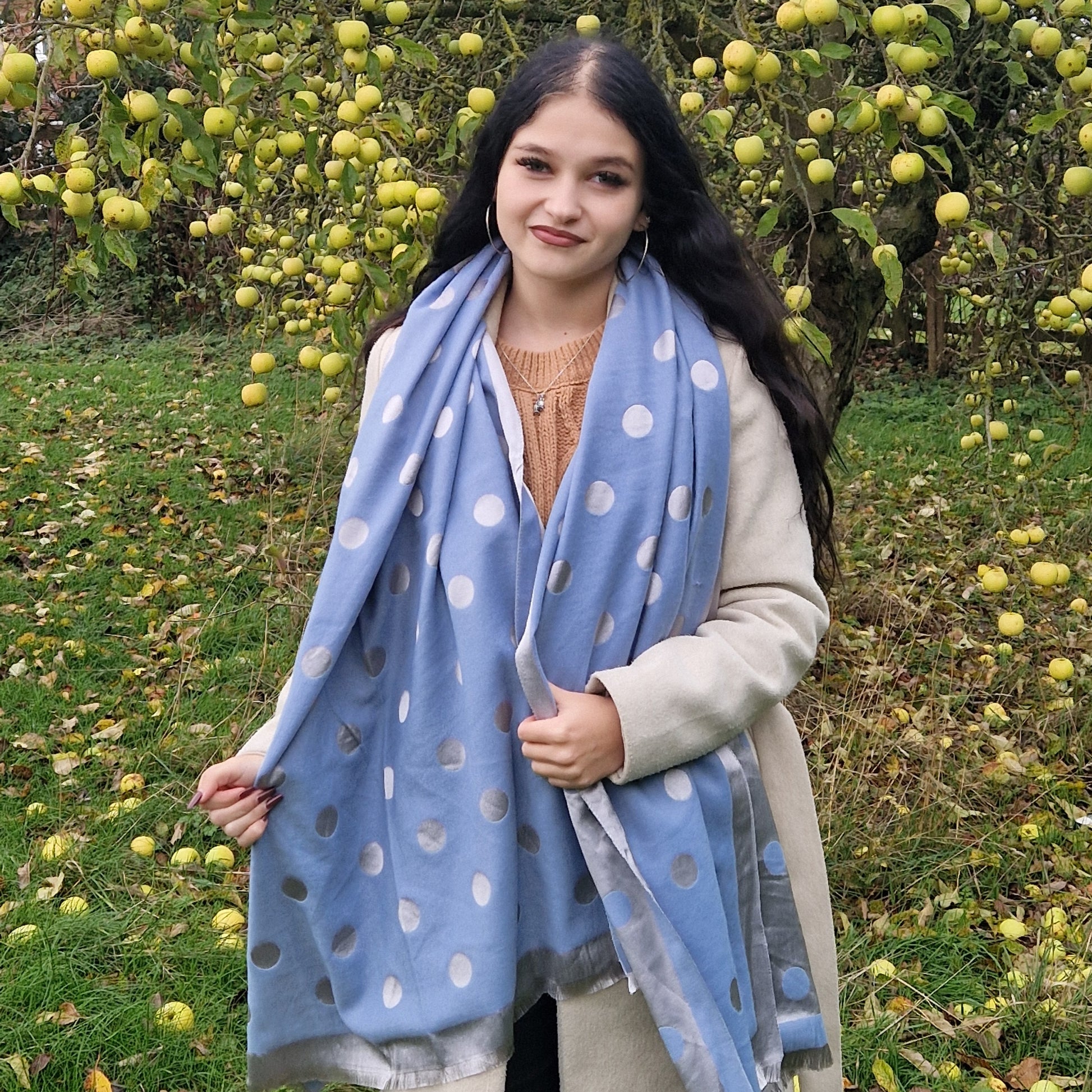 Young Woman wearing a blue polka dot scarf in an outdoor setting with trees and apples.