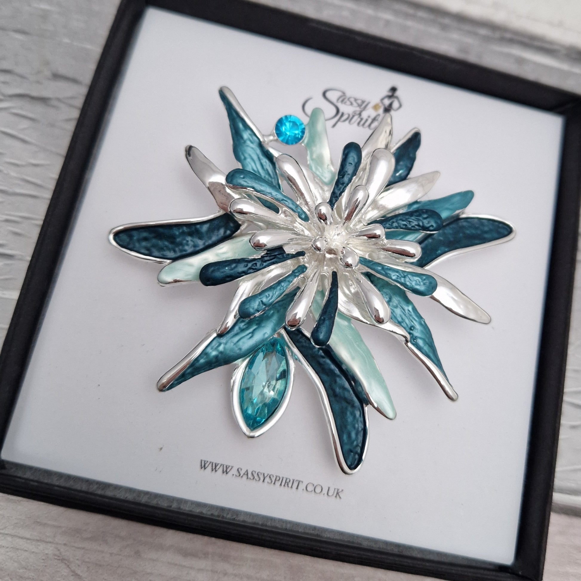Silver and blue floral brooch on a branded display card