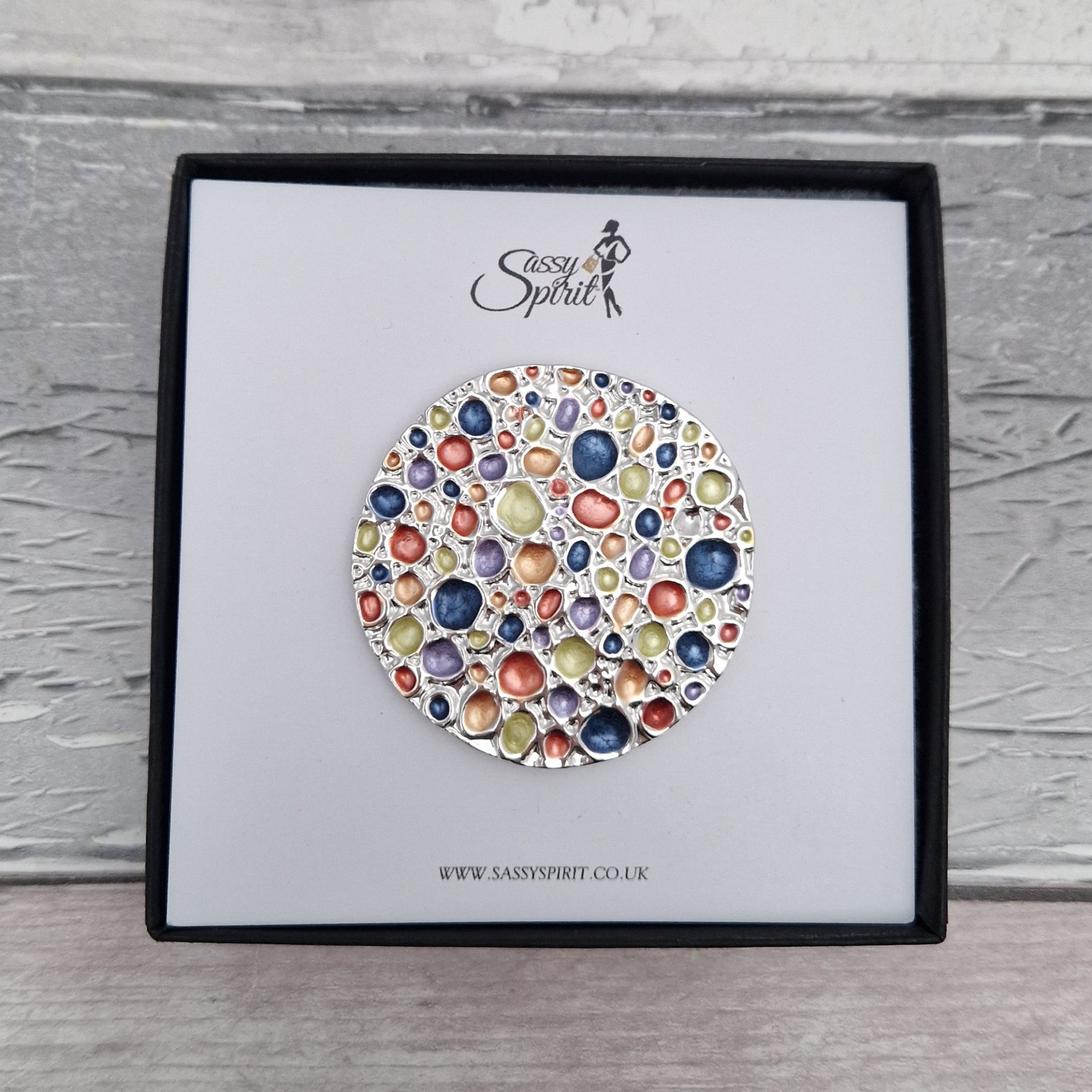 Colorful brooch in a Sassy Spirit box on a wooden surface