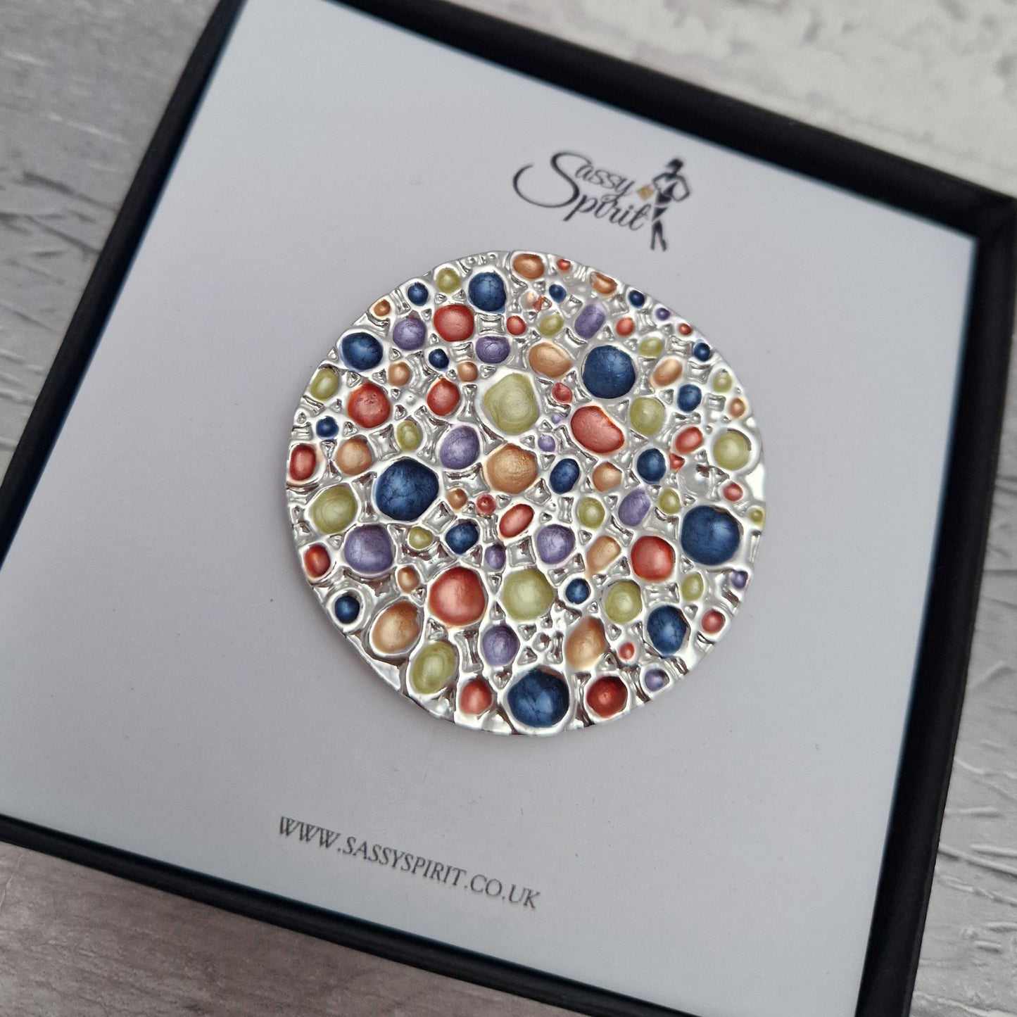 Colorful circular brooch on a branded card with 'Sassy Spirit' logo