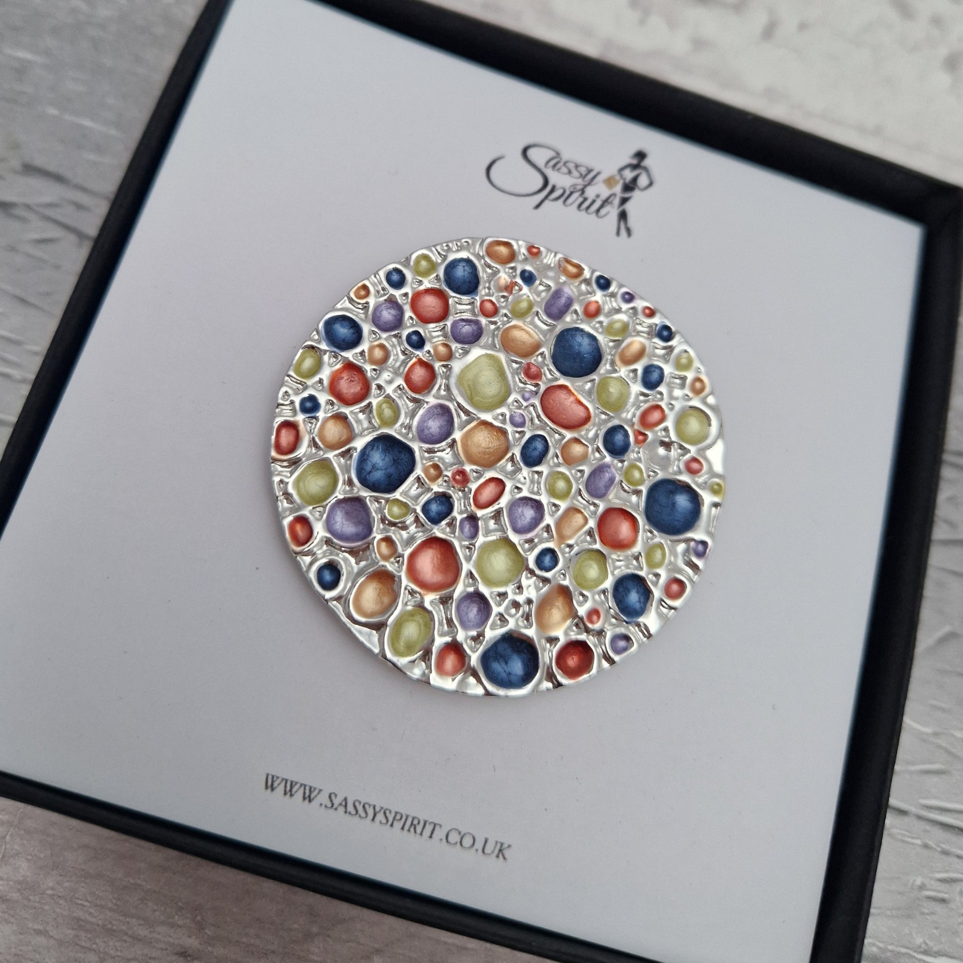 Colorful circular brooch on a branded card with 'Sassy Spirit' logo