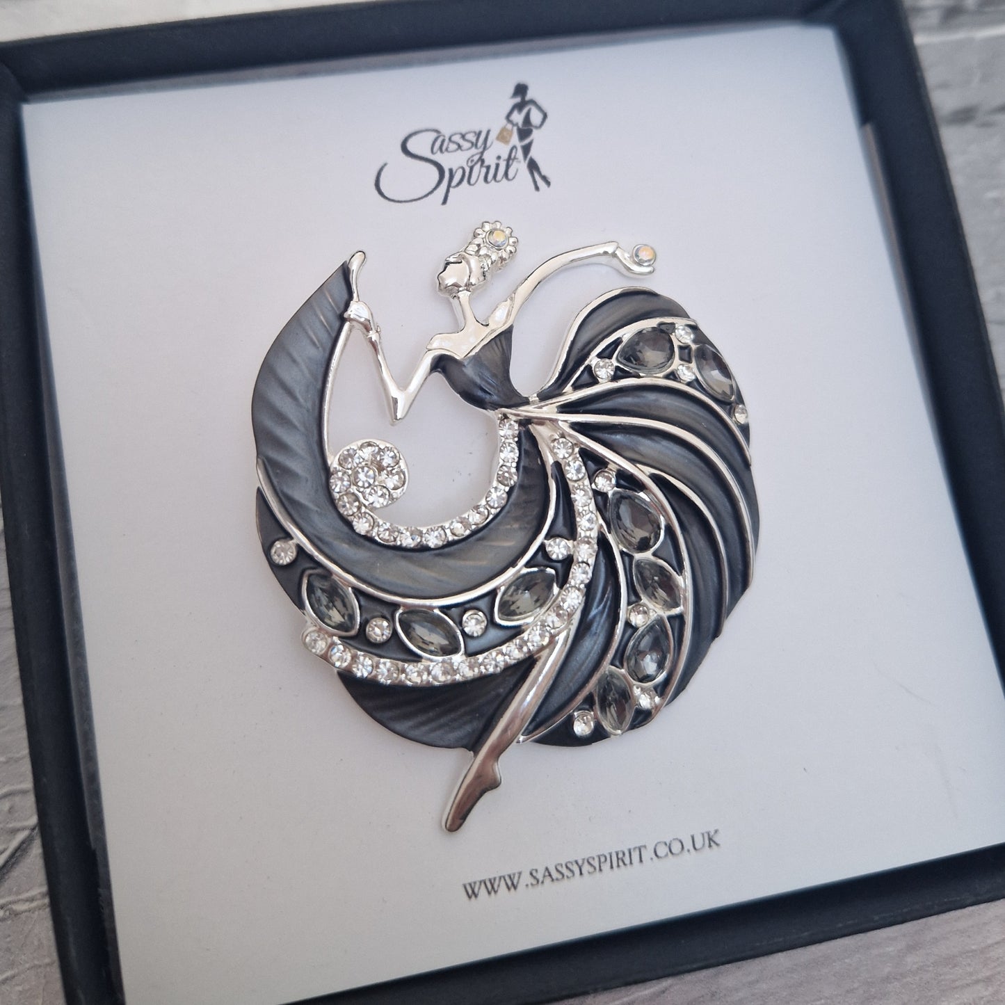 Decorative brooch of a lady in a black gown dancing on a branded display card with 'Sassy Spirit' logo.