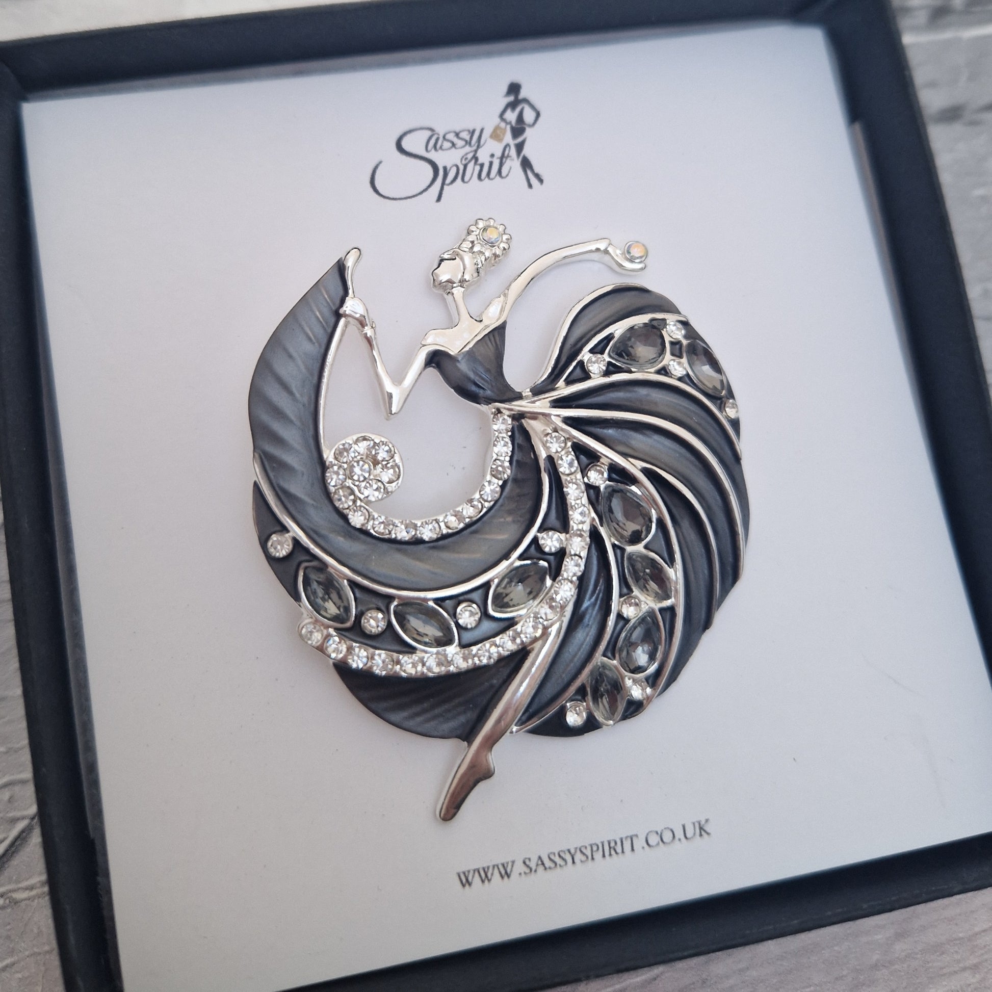 Decorative brooch of a lady in a black gown dancing on a branded display card with 'Sassy Spirit' logo.