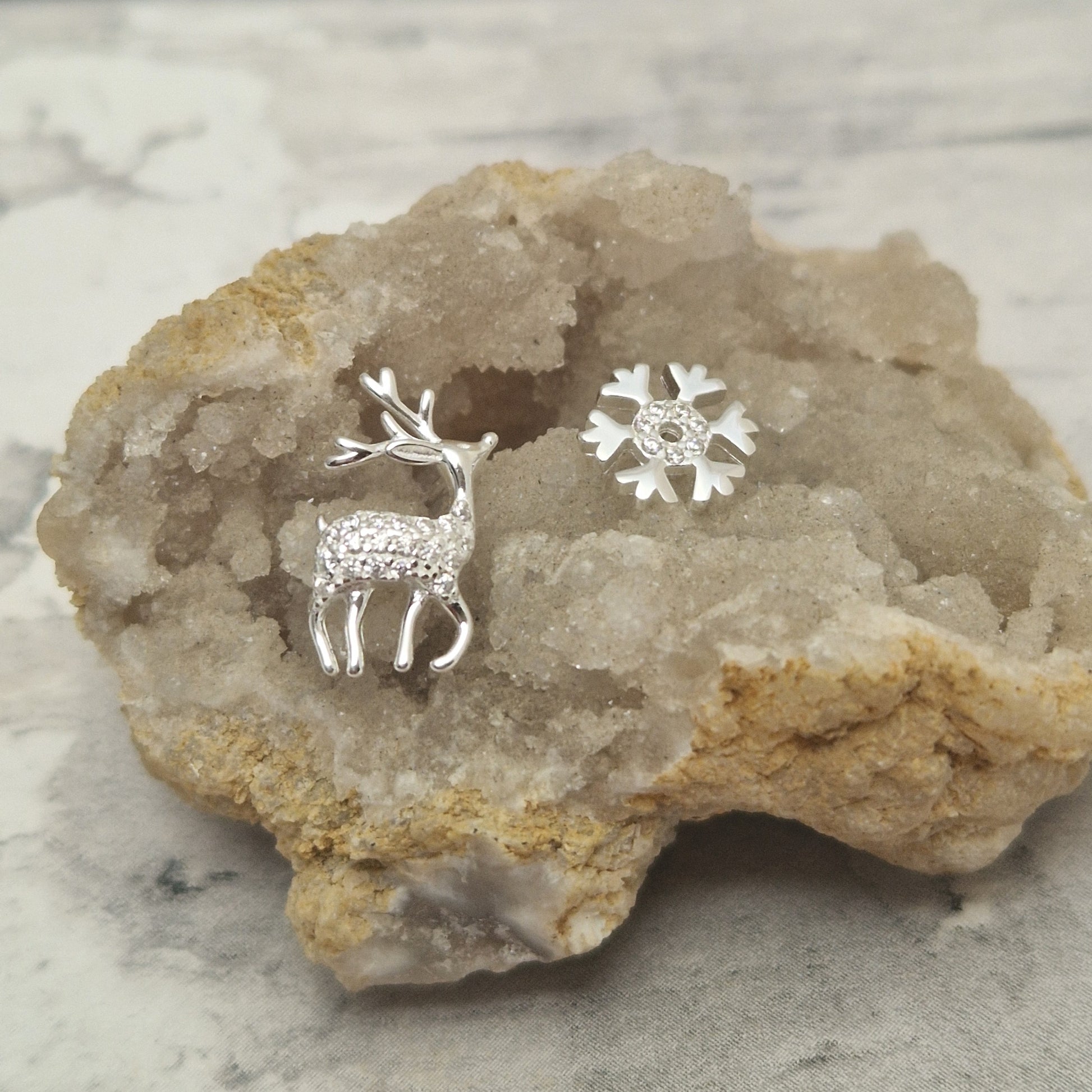 Silver deer and snowflake earrings on a rock with a marble background