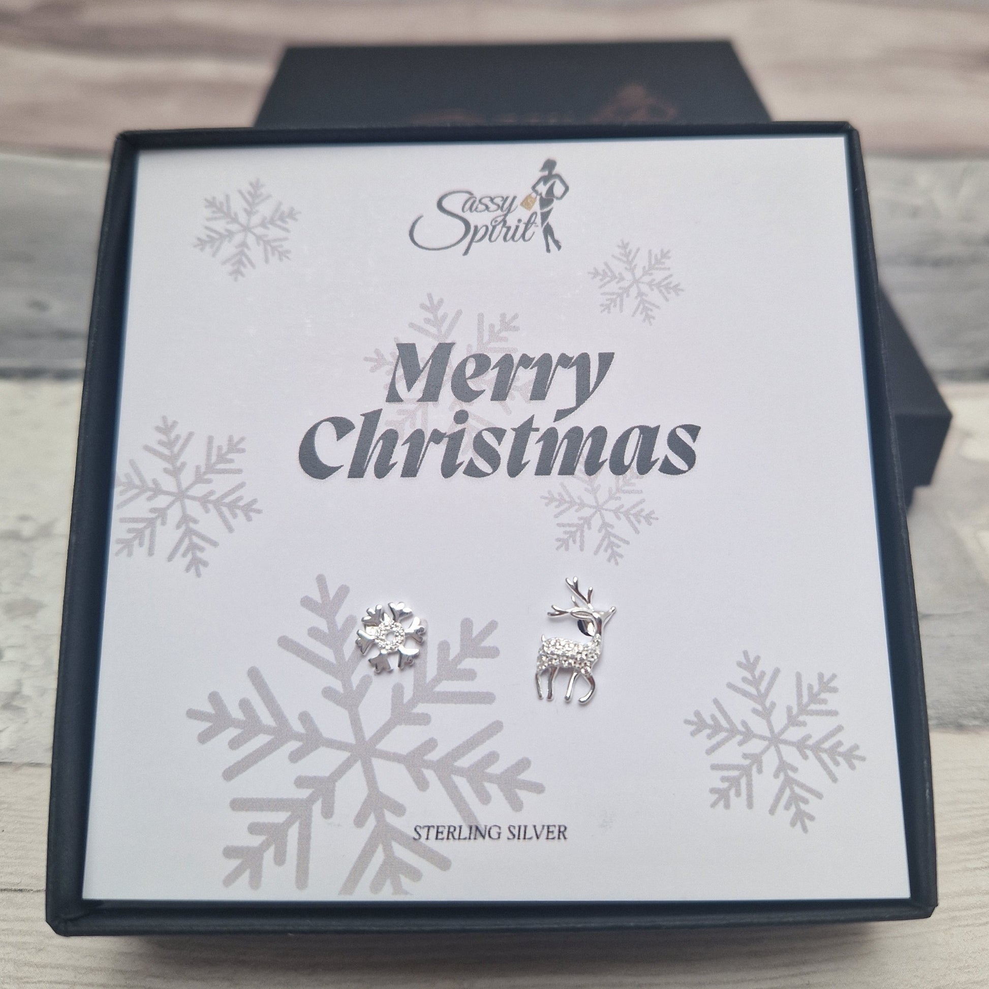 Reindeer and snowflake silver earrings on a 'Merry Christmas' card, featuring snowflakes and 'Sassy Spirit' branding.