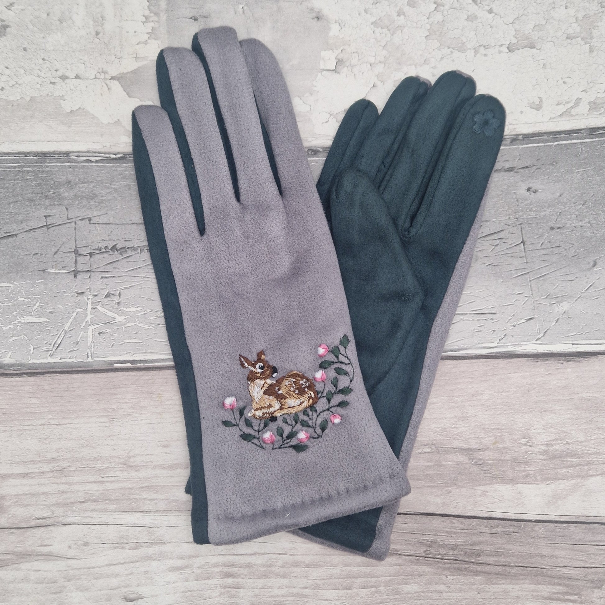 Gray gloves with a embroidered design of a deer and flowers on a wooden surface