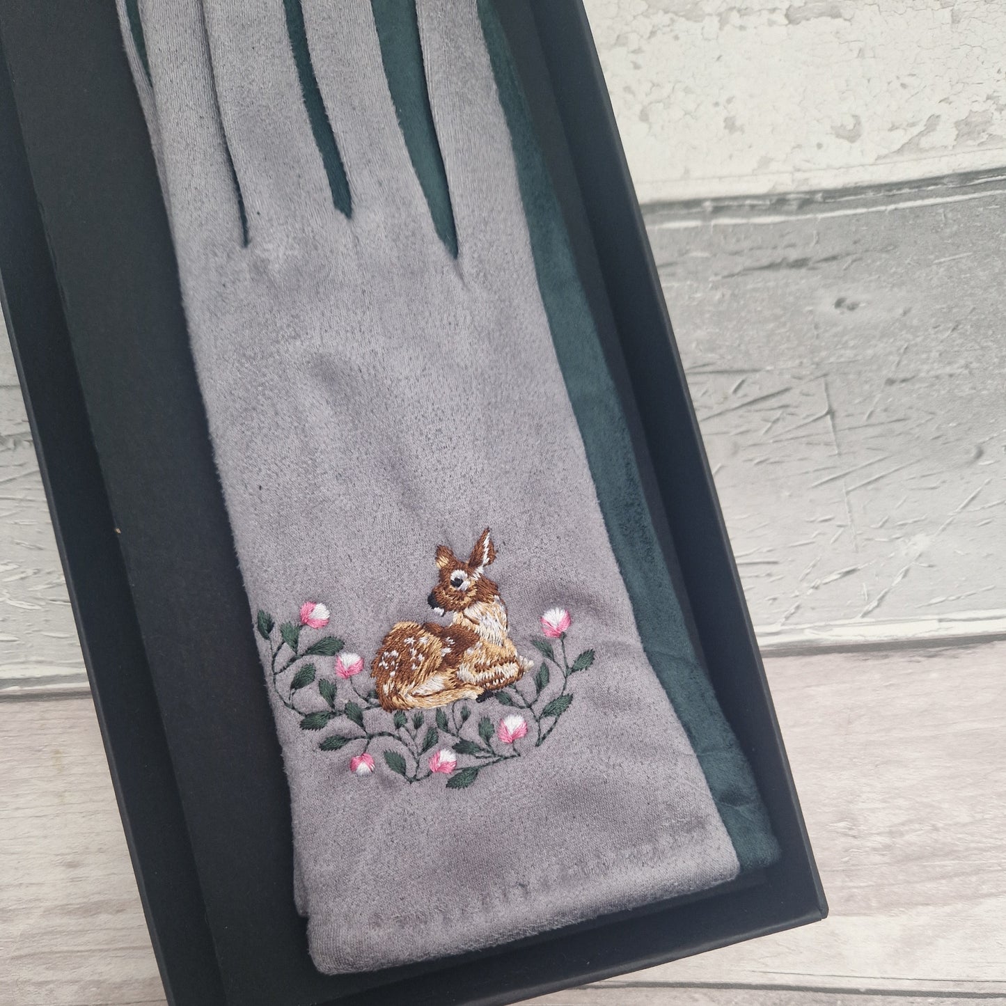 Gray glove with embroidered deer and flowers on a wooden surface
