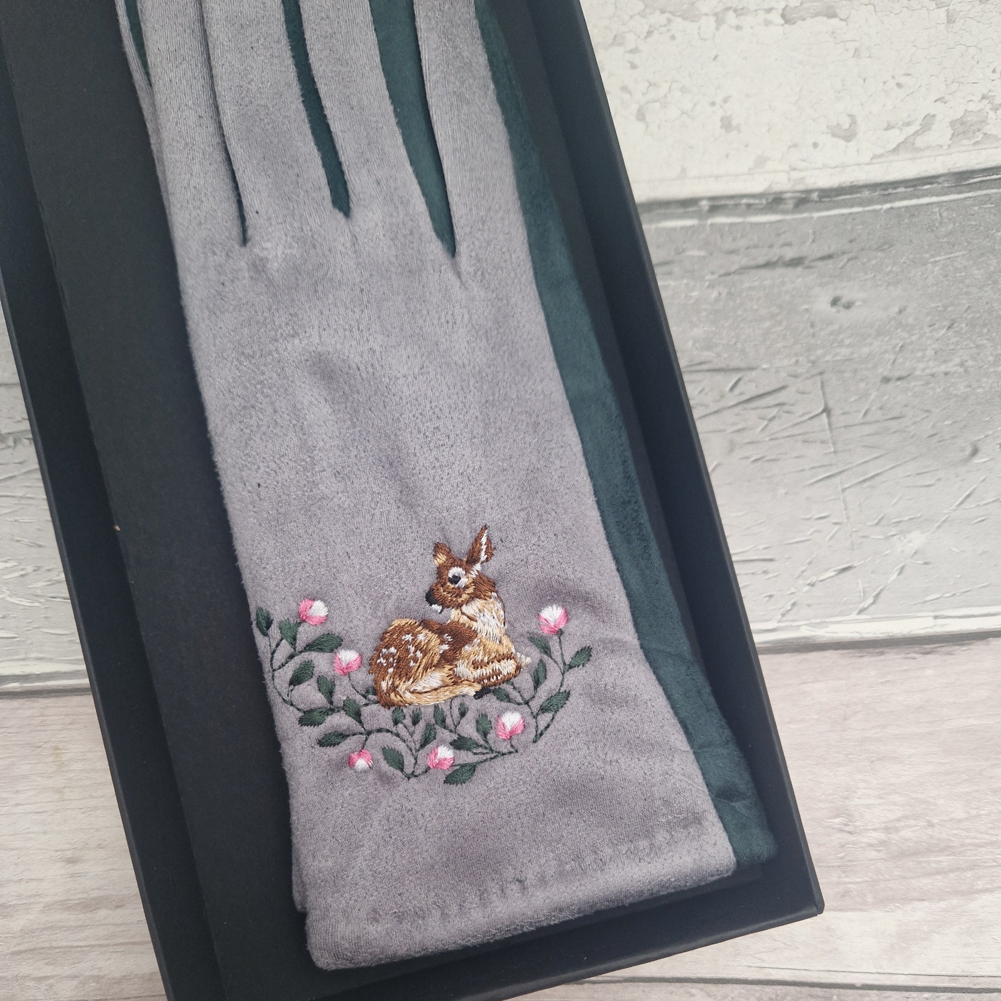 Gray glove with embroidered deer and flowers on a wooden surface