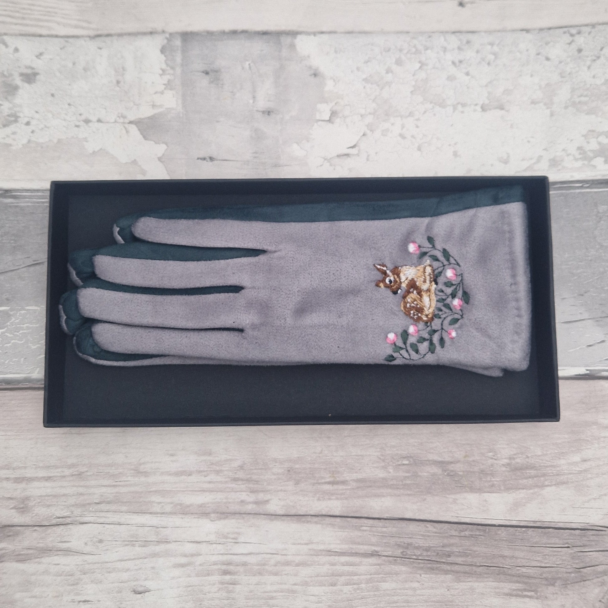 Gray glove with embroidered deer and flowers on a wooden surface