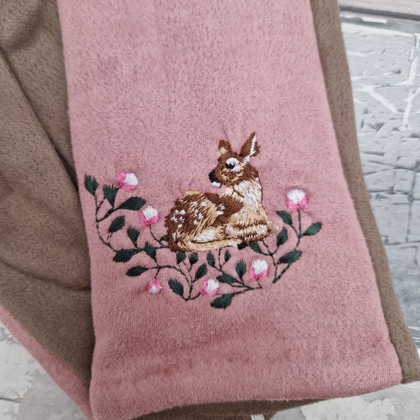 Gray glove with embroidered deer and flowers on a wooden surface