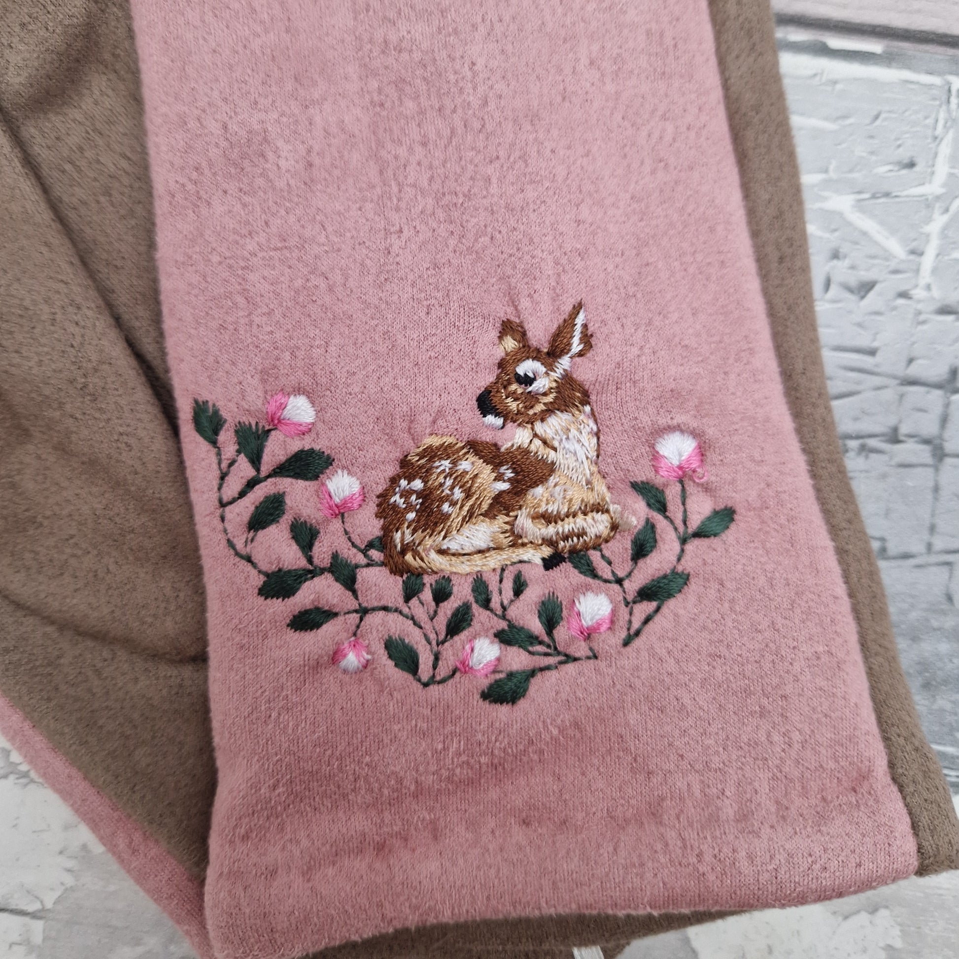 Gray glove with embroidered deer and flowers on a wooden surface