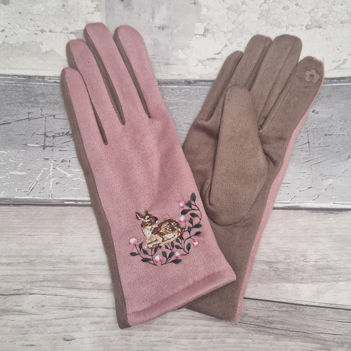 Pink glove with embroidered deer and flowers on a wooden surface