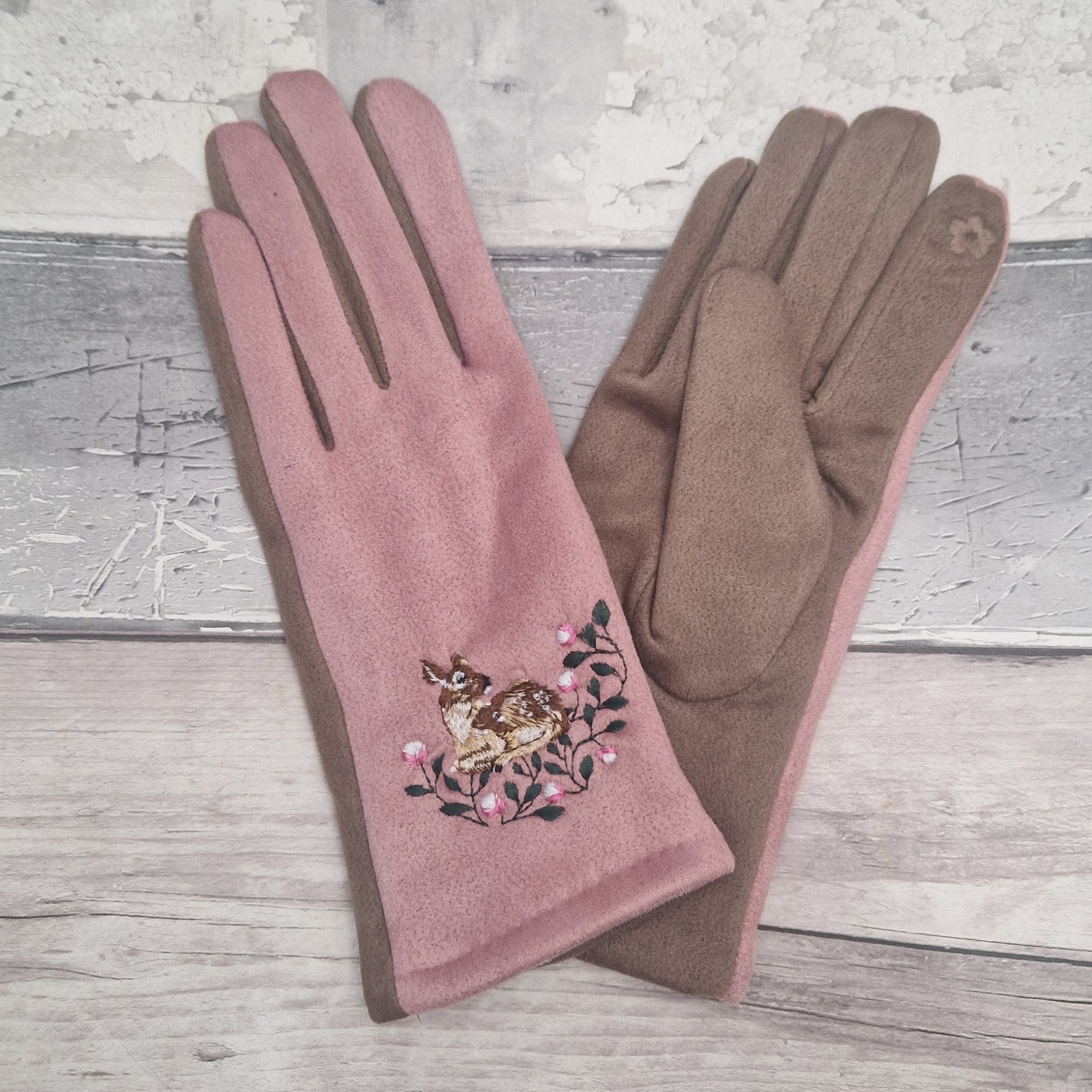 Pink glove with embroidered deer and flowers on a wooden surface