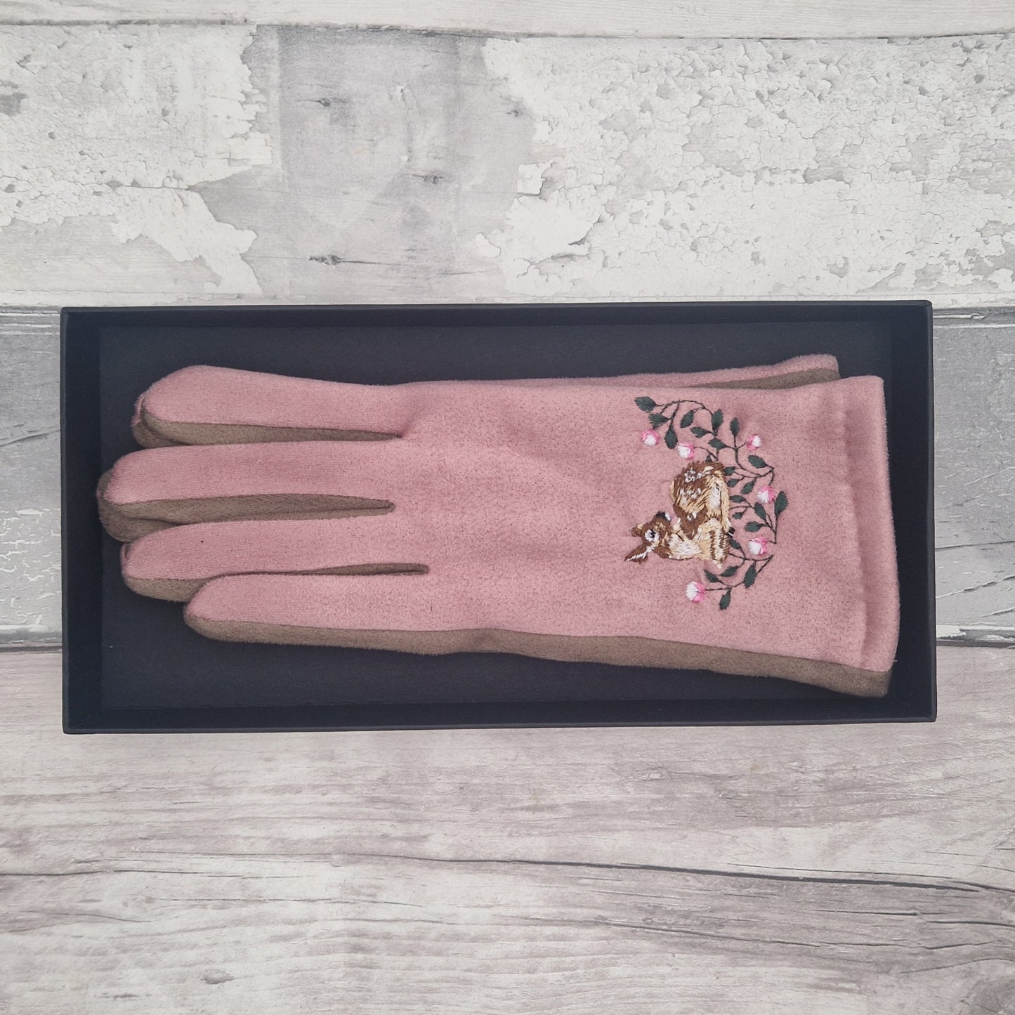 Pink glove with floral and animal design on a black tray against a light wooden background