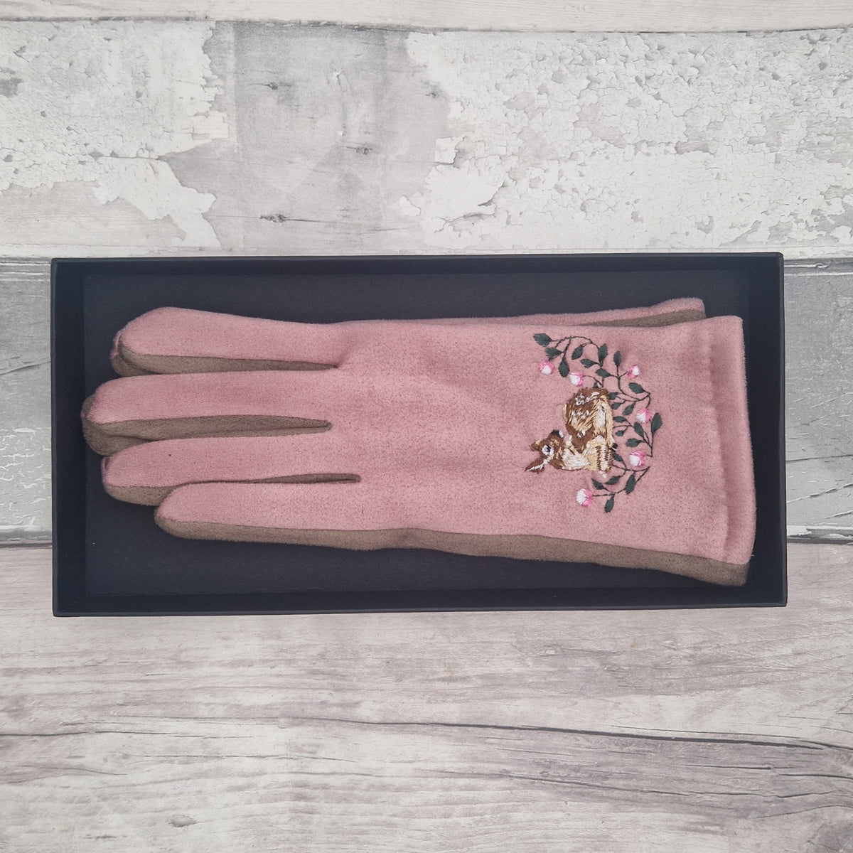 Pink glove with floral and animal design on a black tray against a light wooden background