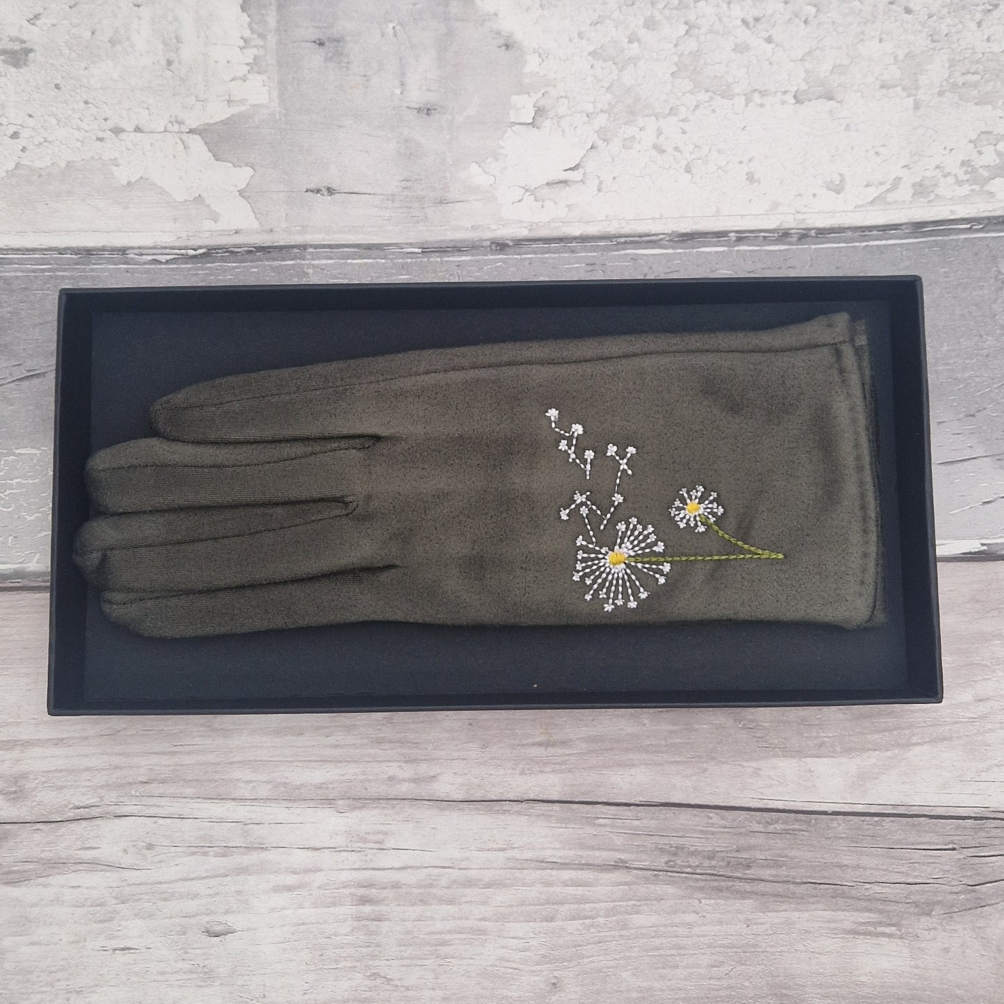 Olive green glove with dandelion embroidery on a black box against a wooden surface
