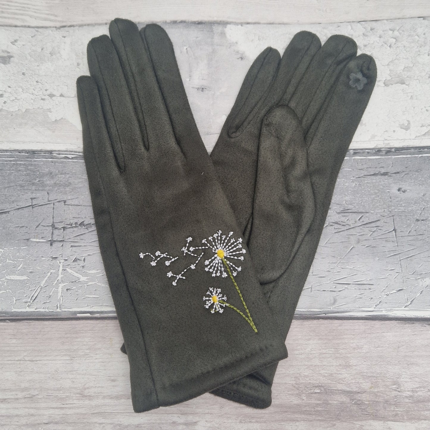 Pair of olive green gloves with dandelion embroidery on a textured surface