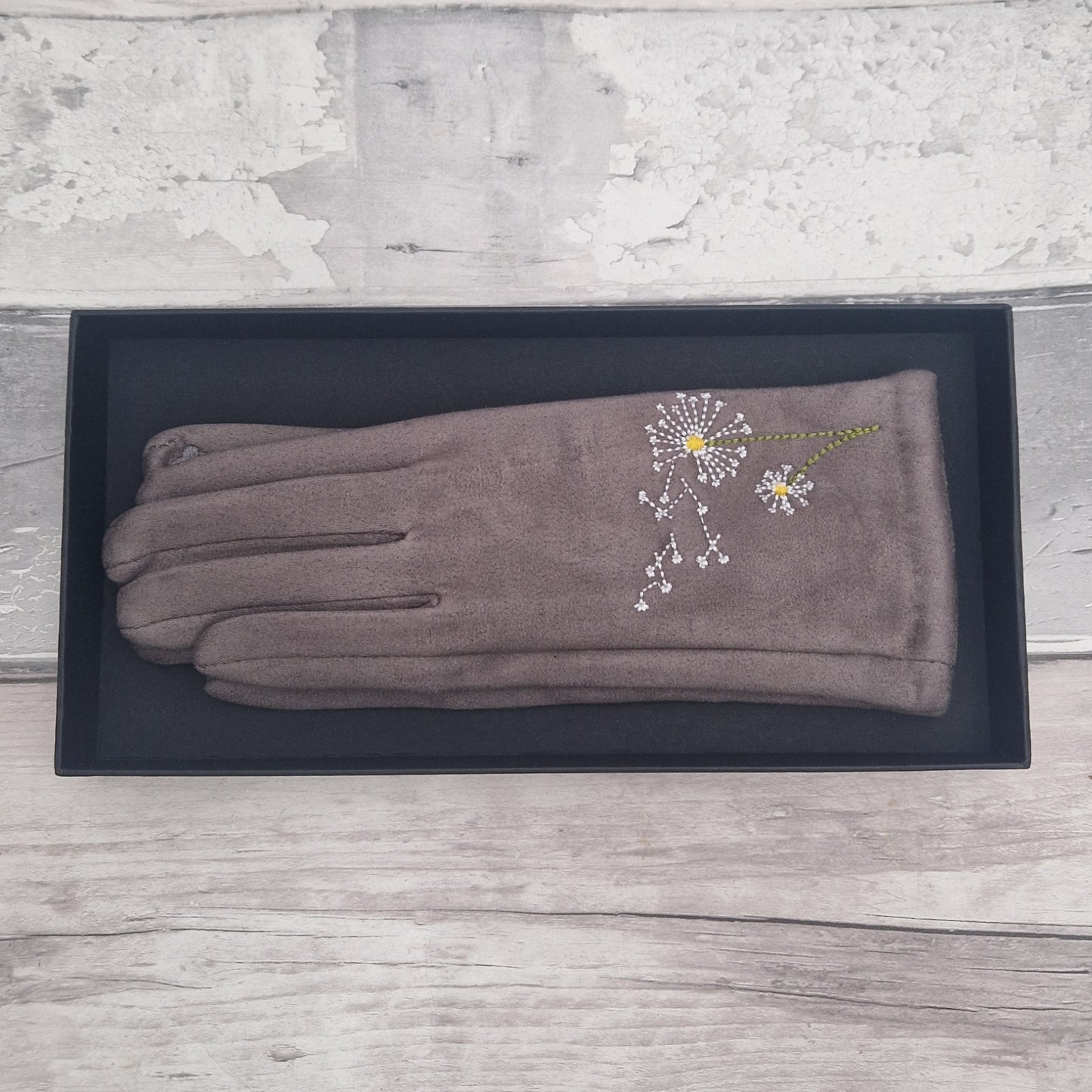 Pair of gray gloves with a dandelion clocks design on a black box against a wooden background