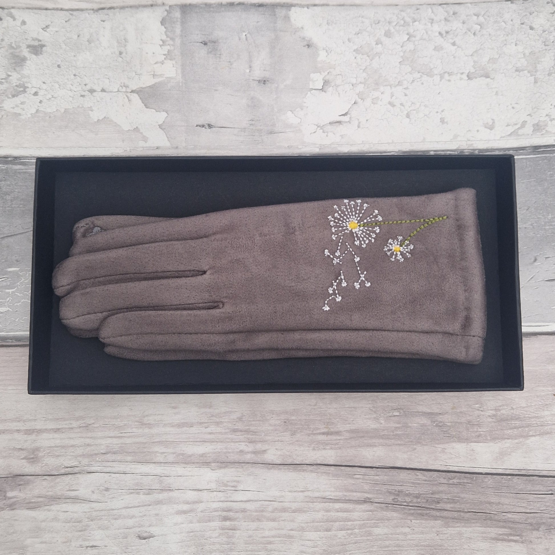 Pair of gray gloves with a dandelion clocks design on a black box against a wooden background