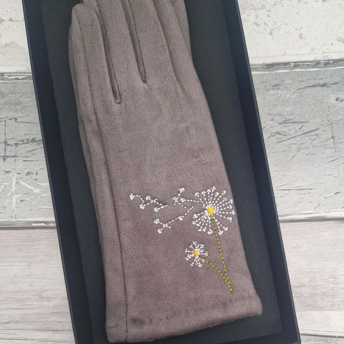 Gray glove with embroidered dandelion design on a wooden surface