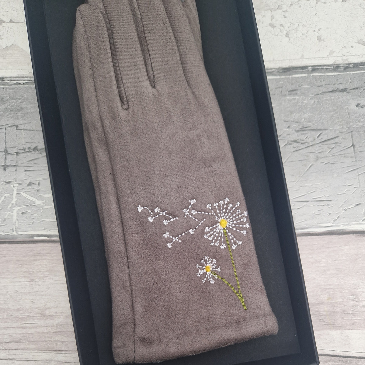 Gray glove with embroidered dandelion design on a wooden surface