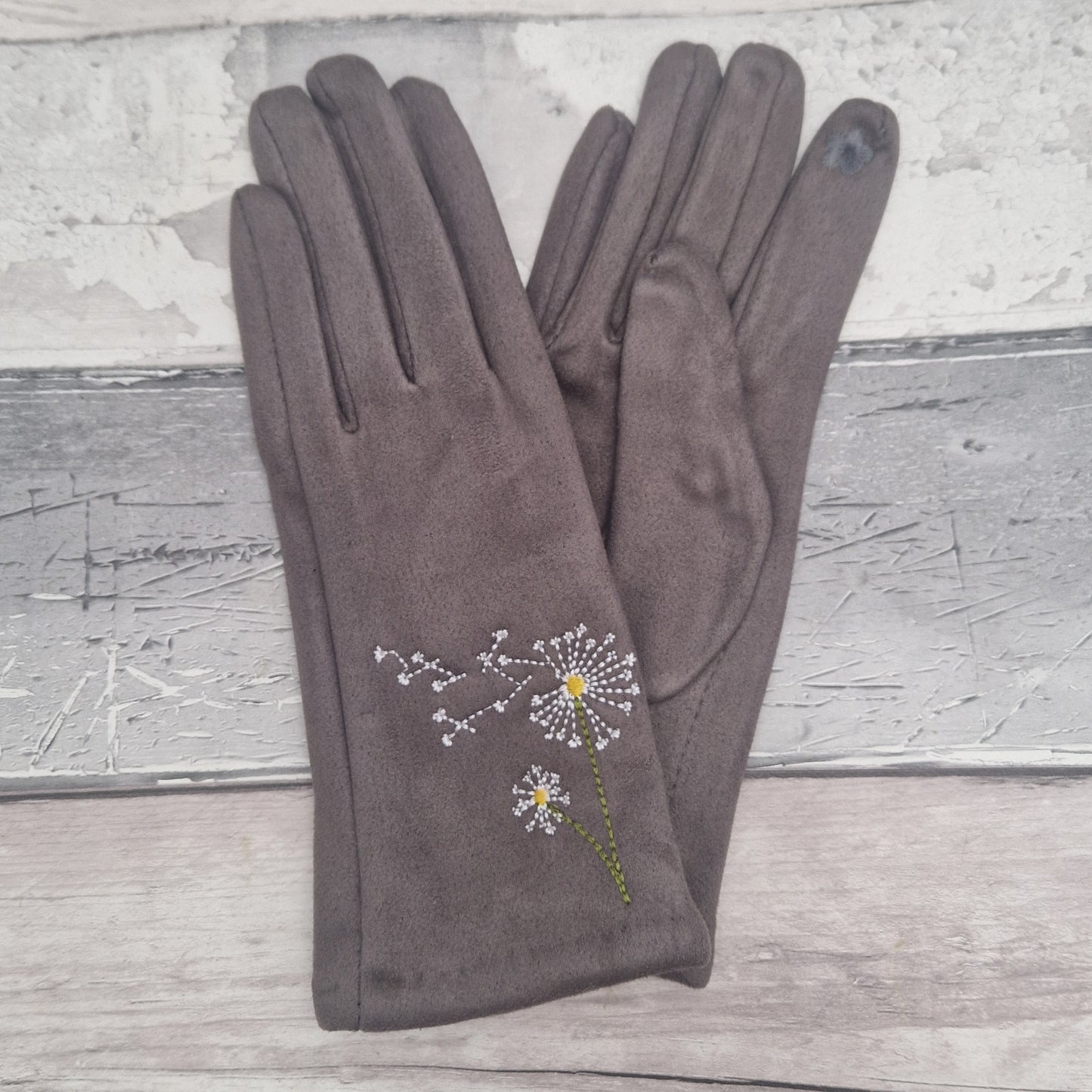 Pair of grey gloves with dandelion embroidery on a wooden surface