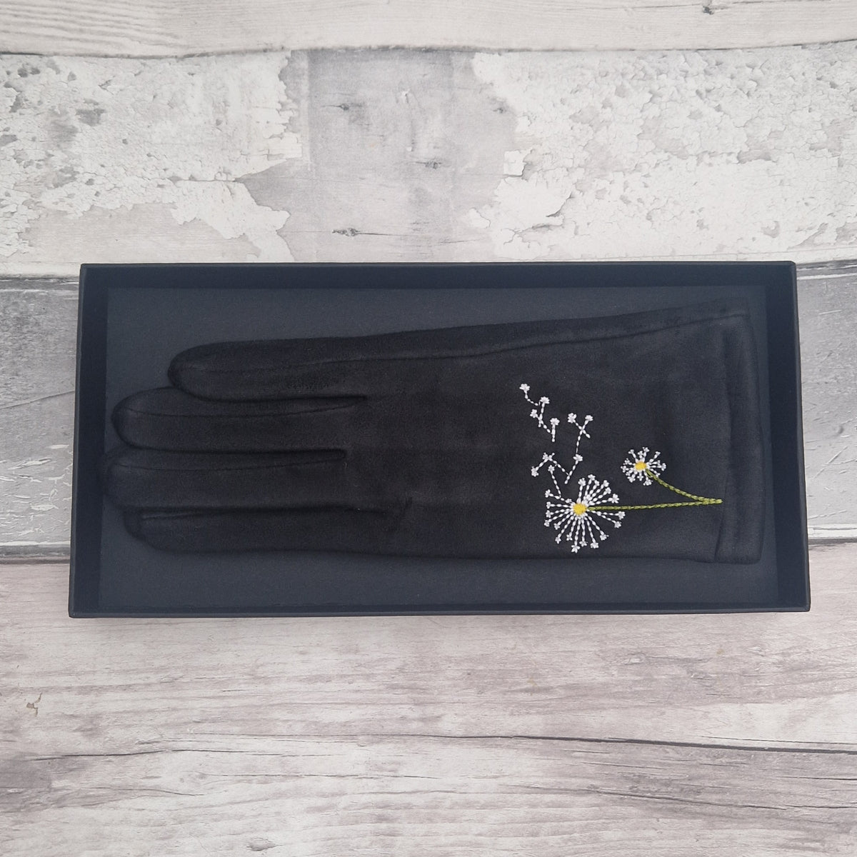 Black glove with dandelion embroidery on a gray wooden surface