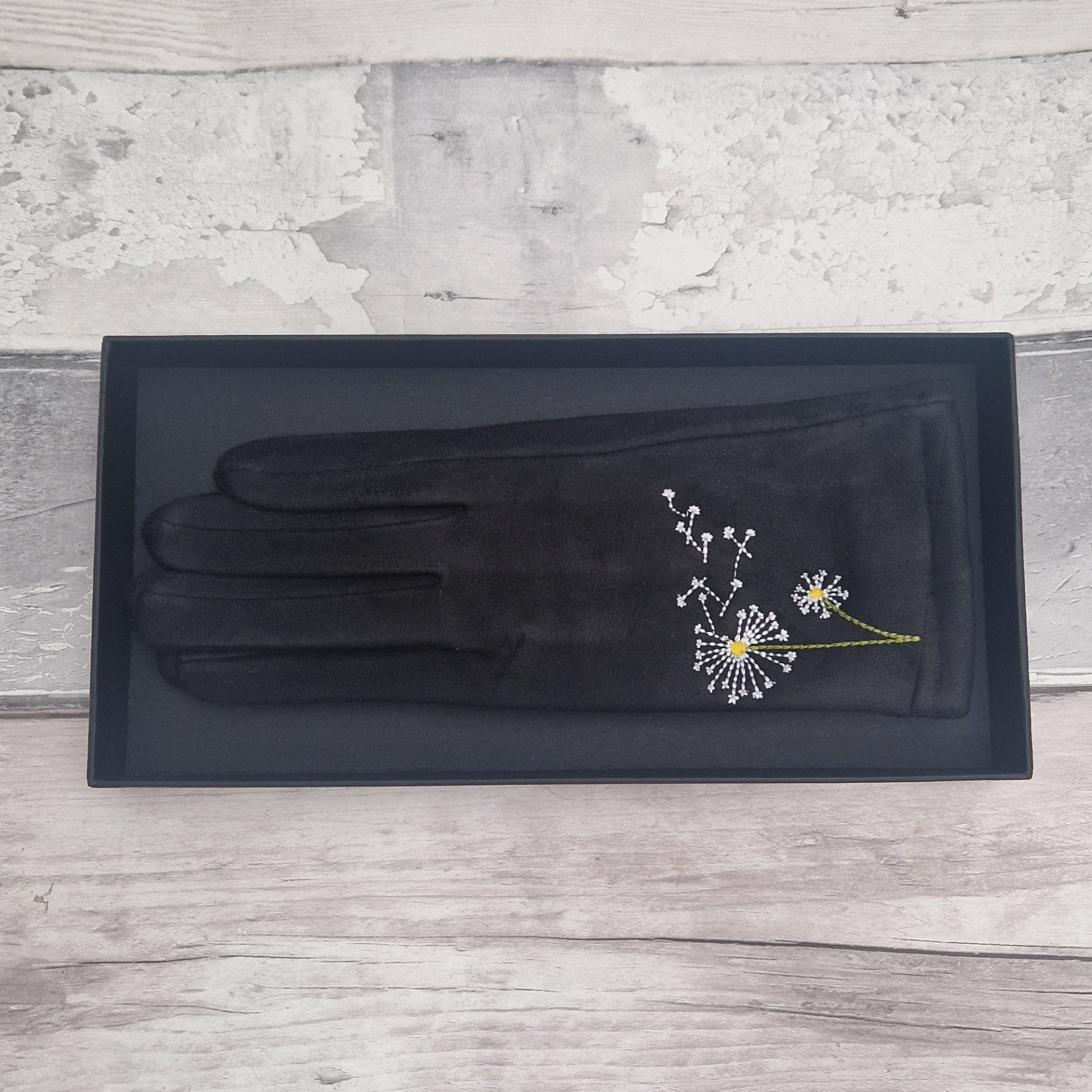 Black glove with dandelion embroidery on a gray wooden surface