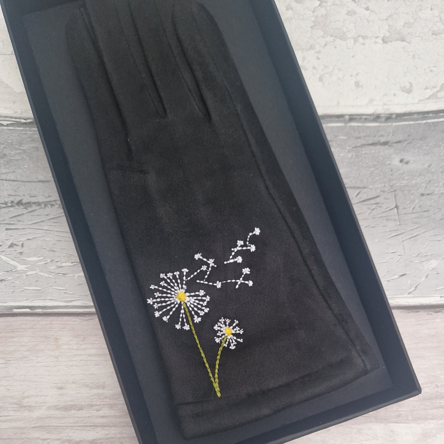 Black gloves with dandelion embroidery in a black box on a wooden surface