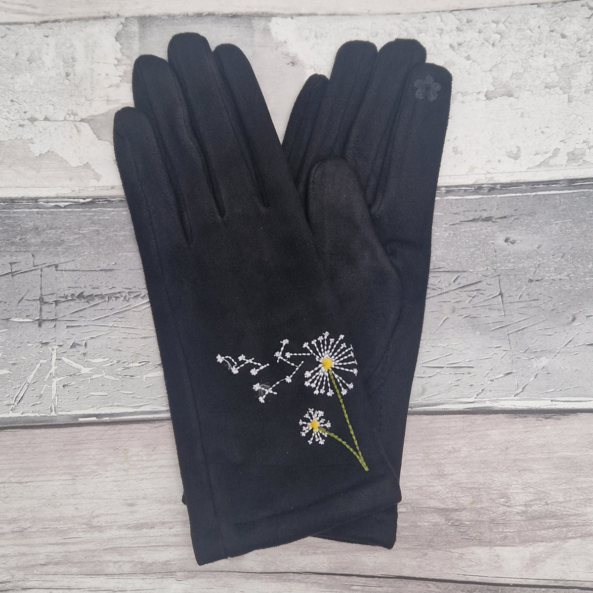 Black gloves with dandelion embroidery on a wooden surface