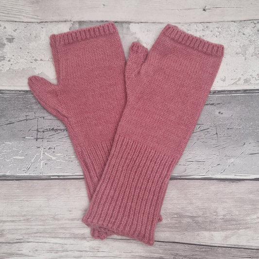 A pair of dusty rose pink knit fingerless gloves laid flat on a rustic, light gray weathered wood plank background.