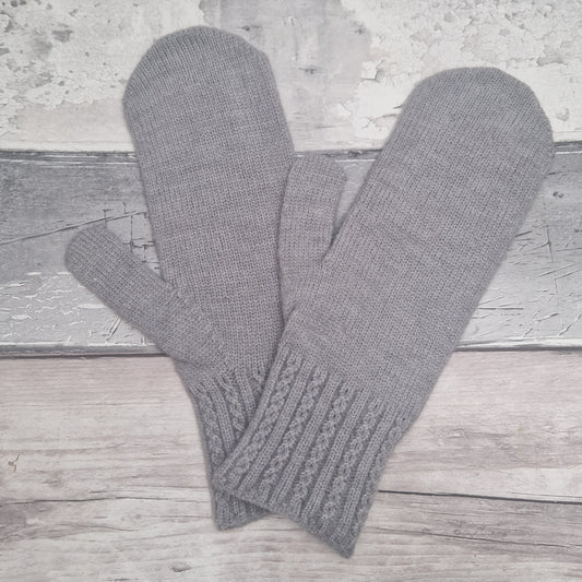 A pair of gray knit fingerless mittens with ribbed cable-knit cuffs, displayed on a rustic light gray wooden surface.