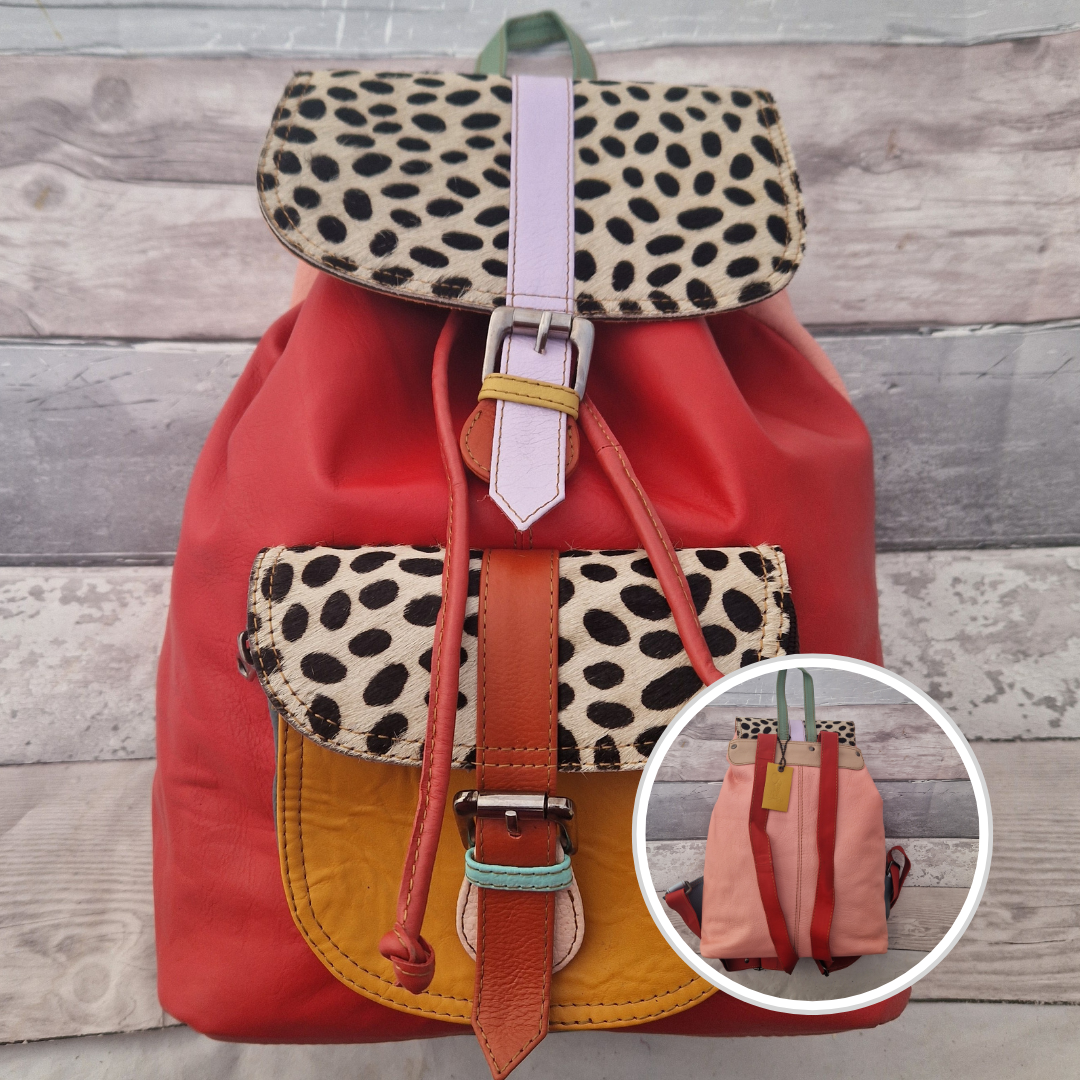 Multicolored backpack made from leather with front pocket and magnetic buckle closers. Red, orange and textured panels of a black and white spot print.