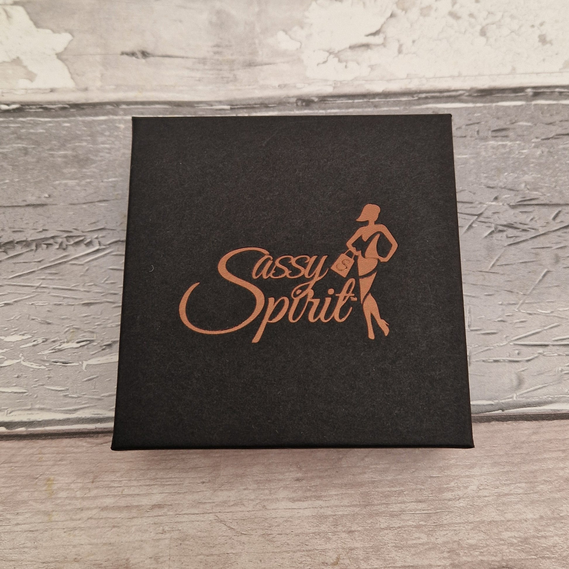 Black gift box with 'Sassy Spirit' logo on a textured surface