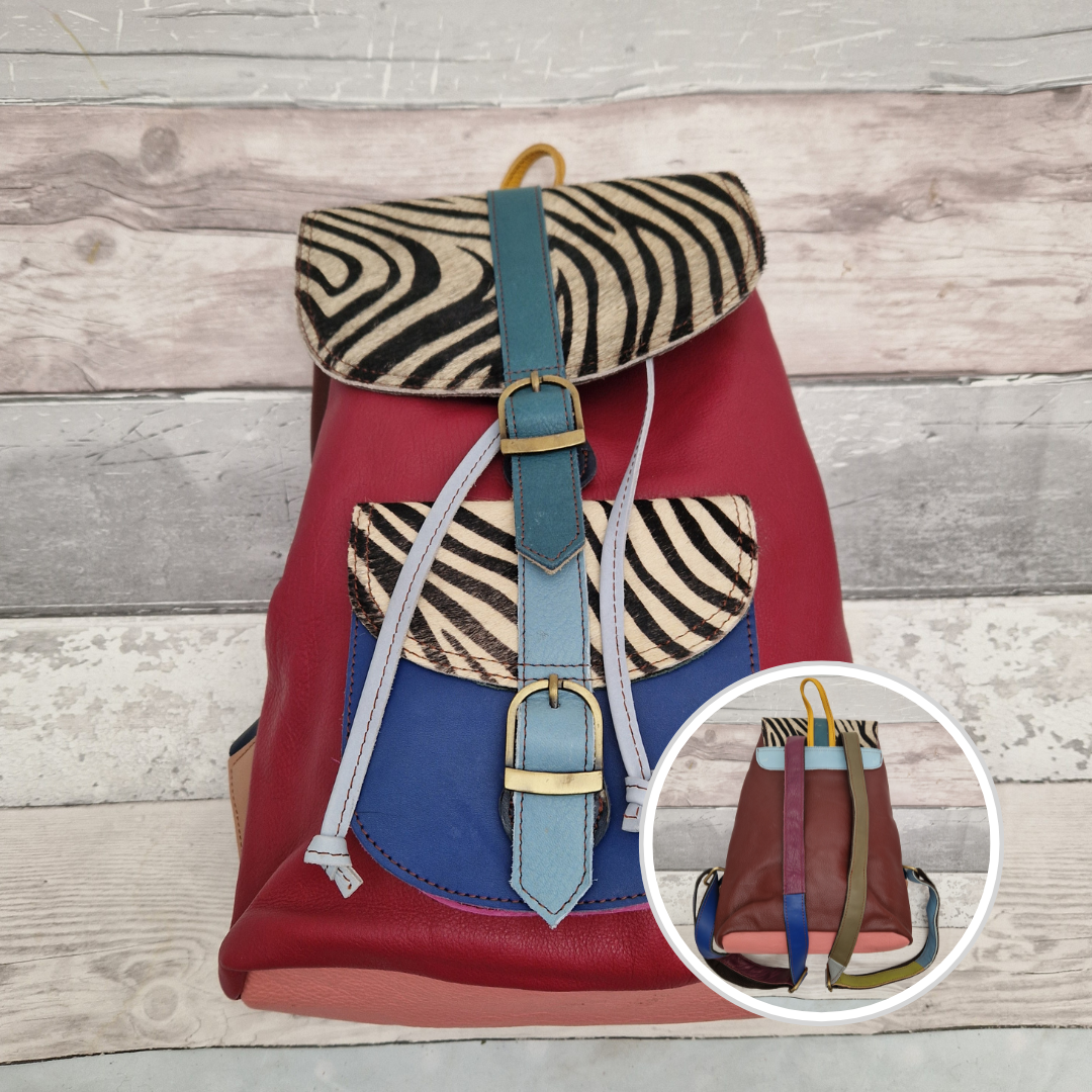 Multicolored backpack made from leather with front pocket and magnetic buckle closers. Burgundy and blue colours with textured zebra print panels.