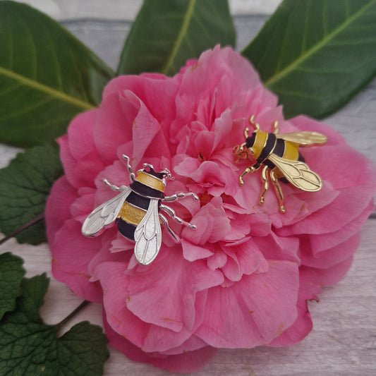 Two bee-shaped Brooches on a pink flower with green leaves.